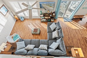 A spacious living room with a large sectional sofa, a ceiling fan, and a television mounted on the wall.