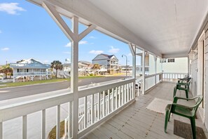 A covered porch with a view of a street and houses.
