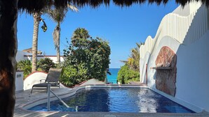 Área de piscina con vista al océano, rodeada de palmeras y una estructura de techo de paja.