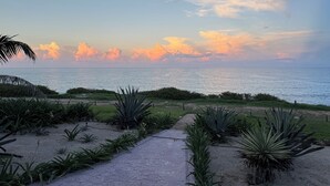 Un camino pavimentado que lleva a una playa con vistas al océano y al atardecer.