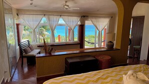 Una habitación de hotel con cama, un banco, una mesita y vistas al océano.