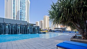 Un espace piscine aménagé sur le toit, avec des chaises longues bleues et un élément décoratif aquatique.