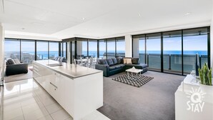 Un salon moderne avec une grande fenêtre, un canapé, une table basse et un coin cuisine.