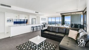 Un salon moderne avec un canapé en cuir noir, une table basse blanche et un tapis à motifs.