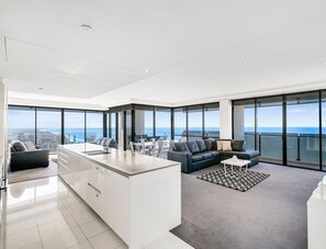 Un salon moderne avec une grande fenêtre, un canapé, une table basse et un coin cuisine.
