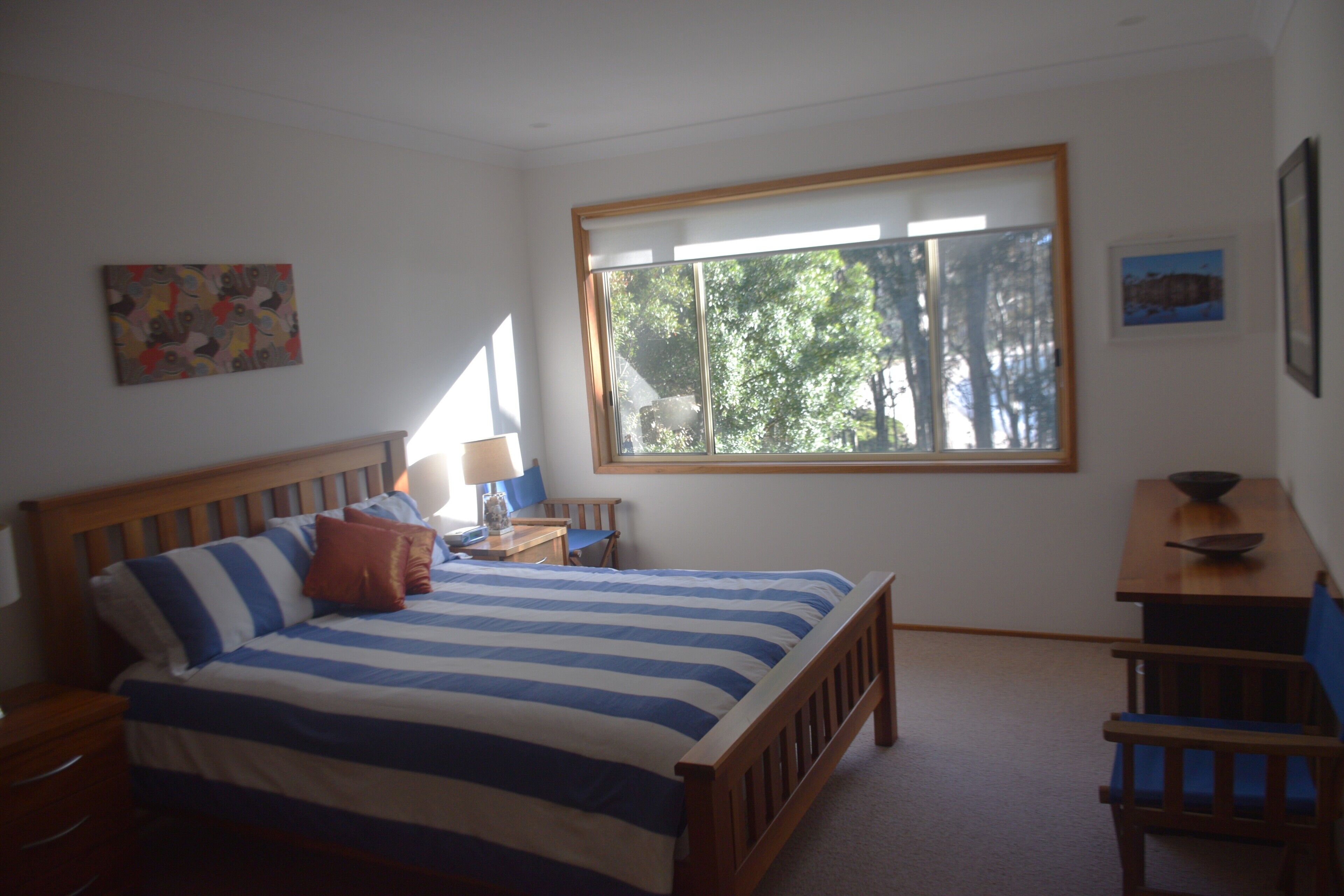 A bedroom with a bed, a desk, a chair, and a window with a view of trees.