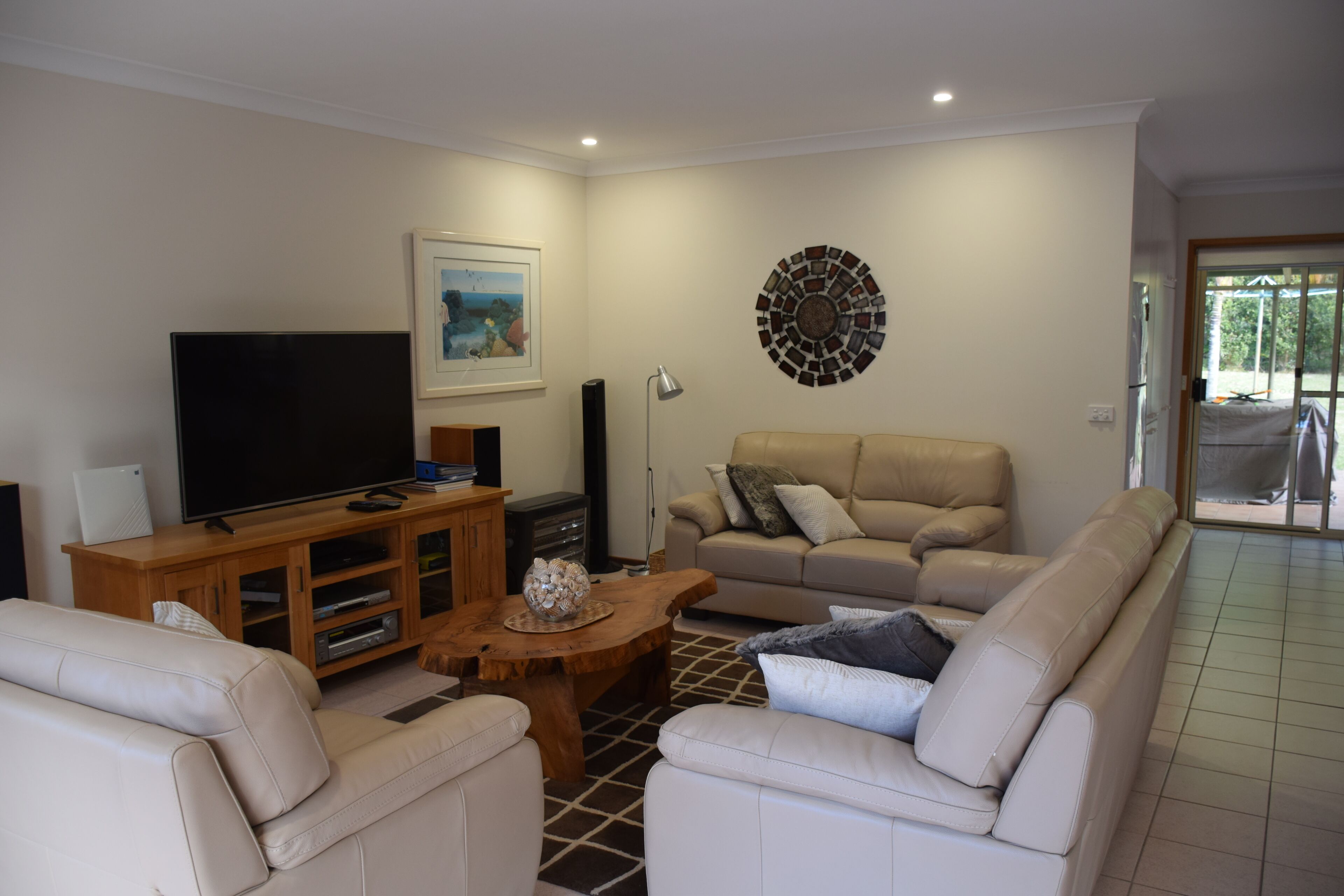 Una sala de estar con televisor de pantalla plana, mueble de madera para entretenimiento, sofá color beige y una alfombra estampada.