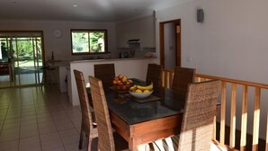 A dining area with a table set for four, surrounded by wicker chairs, and a bowl of fruit on the table. - Beach House - direct 2-min access to the beach (Depot Beach)