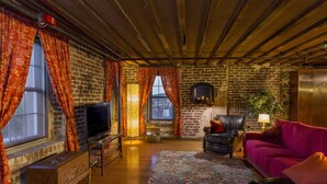 A cozy living room with a brick wall, a television, leather furniture, and a patterned rug. - Rare River Street w/Balcony, Historic, Luxury, Affordable, 2/2, Loft STVR00088 (Savannah)