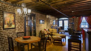 A cozy interior with exposed brick walls, a wooden dining table with chairs, a patterned sofa, and a view through a large window. - Rare River Street w/Balcony, Historic, Luxury, Affordable, 2/2, Loft STVR00088 (Savannah)