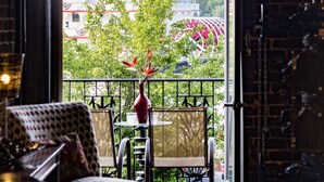 A room with a view of a building with American flags, a patterned chair, and a vase with red flowers. - Rare River Street w/Balcony, Historic, Luxury, Affordable, 2/2, Loft STVR00088 (Savannah)