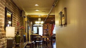 A hallway with a brick wall, wooden floor, and a patterned rug. There are tables and chairs along the wall, and a chandelier hangs from the ceiling. - Rare River Street w/Balcony, Historic, Luxury, Affordable, 2/2, Loft STVR00088 (Savannah)
