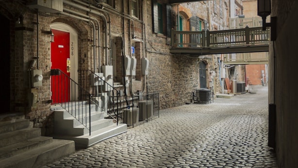 A cobblestone courtyard with a red door, a staircase, and a balcony overlooking a street. - Rare River Street w/Balcony, Historic, Luxury, Affordable, 2/2, Loft STVR00088 (Savannah)