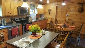 Una cucina in legno con un'isola centrale, pensili in legno, un forno a microonde, un piano cottura e un tavolo da pranzo con sedie.