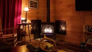 Un accogliente interno di una baita con soffitto in legno, una ventola a soffitto, un caminetto, una televisione appesa al muro e una libreria.