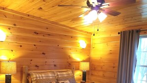 Camera da letto accogliente in legno con un letto, due abat-jour, una ventola a soffitto e una finestra con tende.