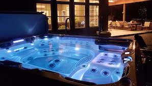 A hot tub with multiple jets, a covered patio area with chairs, and a building with large windows in the background. - Sleeps 27/Pickleball Court/Game Room/Hot Tub/Pool/Batting Cage/Beach (Coxsackie)