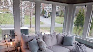 A cozy living room with a grey sofa, a table with a lamp, candles, and a view of a suburban street. - Sleeps 27/Pickleball Court/Game Room/Hot Tub/Pool/Batting Cage/Beach (Coxsackie)