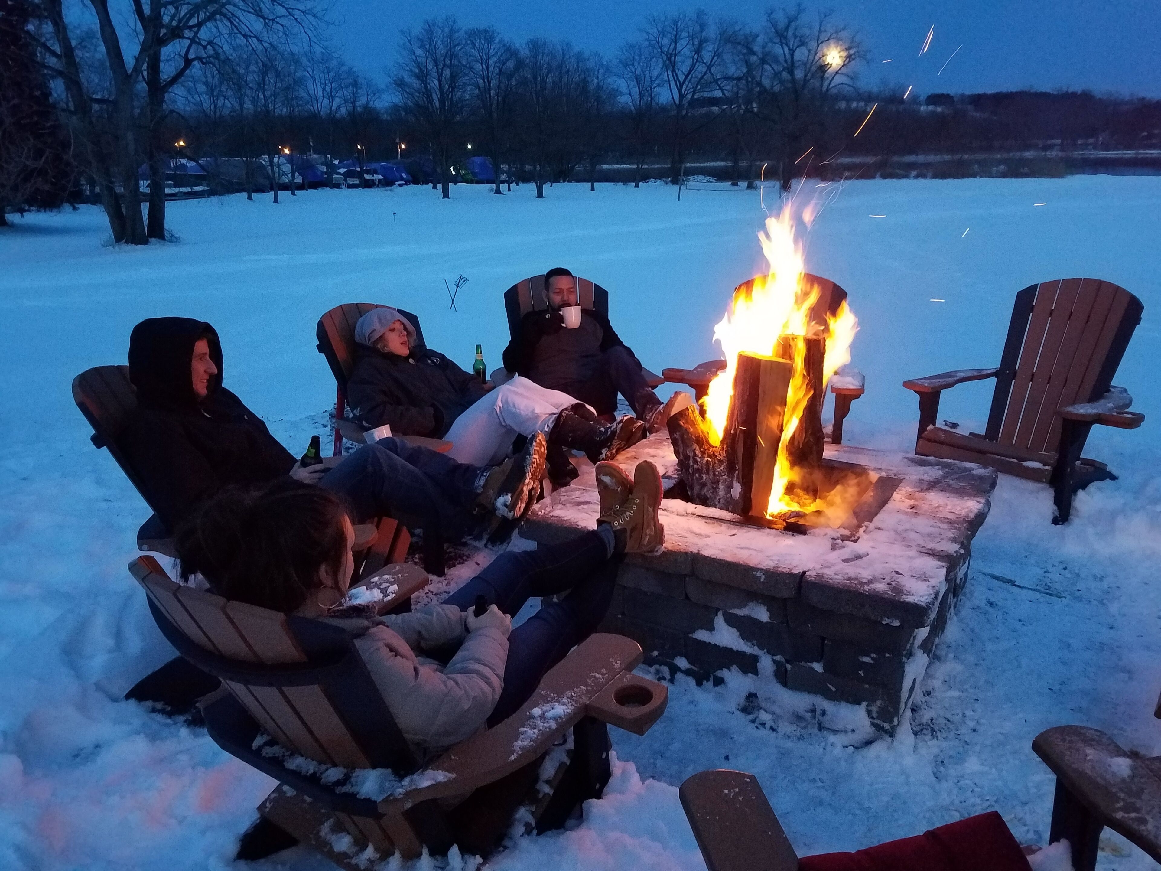 Un grupo de personas sentadas alrededor de un brasero en un entorno nevado al aire libre.