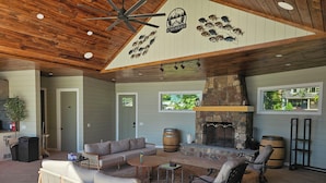 A covered outdoor living area with a stone fireplace, seating arrangements, and a ceiling fan. - Sleeps 27/Pickleball Court/Game Room/Hot Tub/Pool/Batting Cage/Beach (Coxsackie)