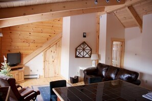 Ein gemütliches Wohnzimmer mit Holzboden, einer Ledersofa, einem Fernseher und einer kleinen Weihnachtstanne.