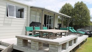 A mobile home with a patio area featuring a wooden table and chairs, a covered barbecue grill, and a carport with a covered car. - Destination Matapouri (Matapouri)