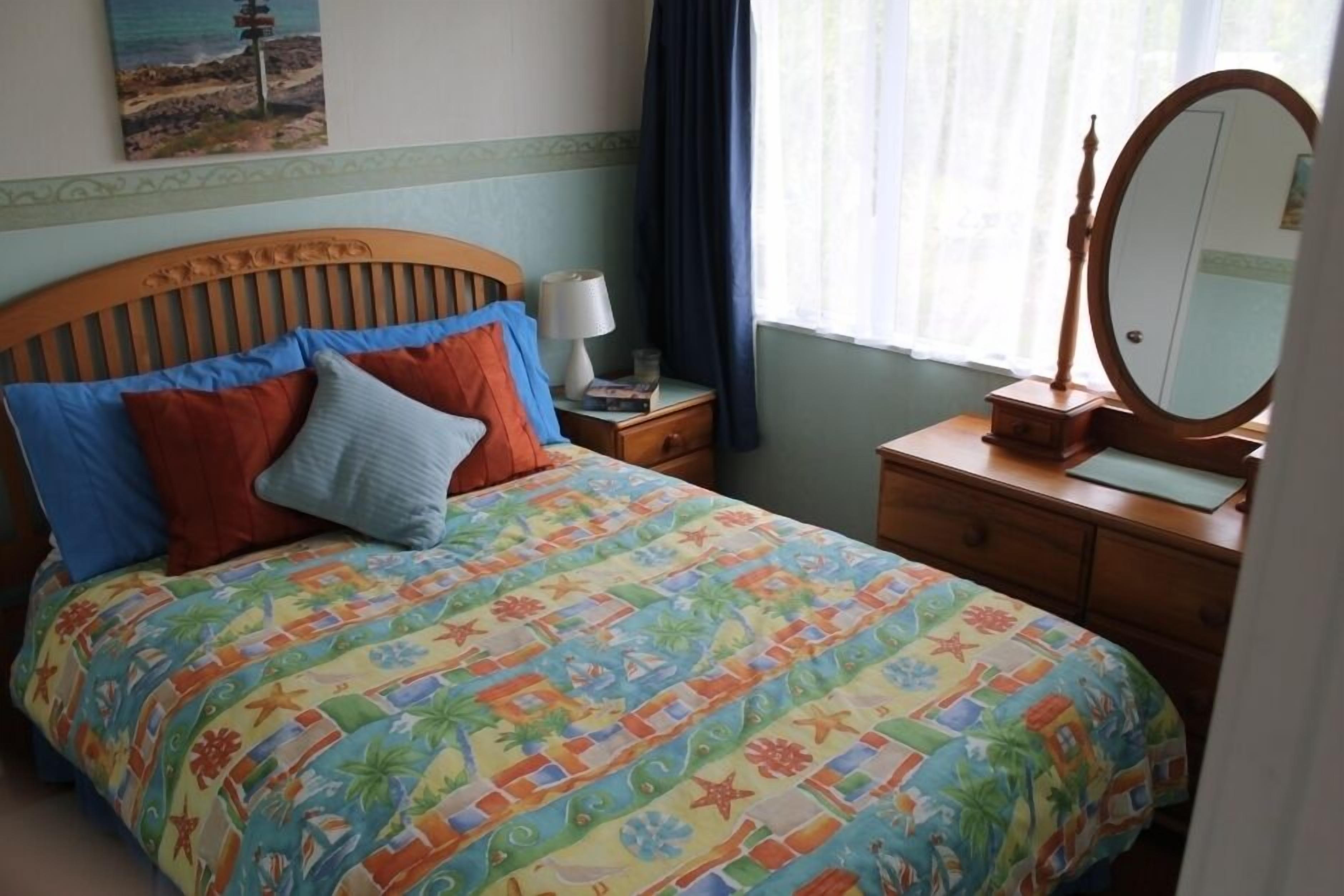 Una camera da letto con un letto, un comodino, una cassettiera, uno specchio e una finestra con tende.