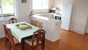 A compact kitchen with a dining area, a refrigerator, and a microwave. - Destination Matapouri (Matapouri)