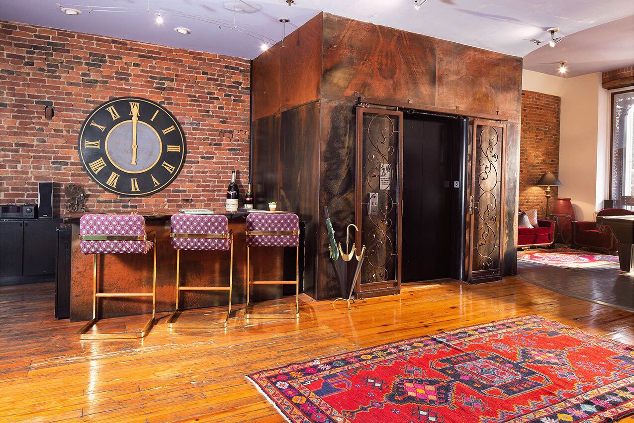 A bar area with a large clock, wooden bar counter, and patterned stools.