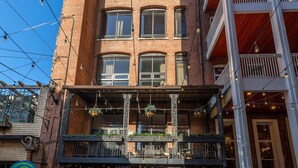 Un immeuble à plusieurs étages avec une façade en briques, un café situé au rez-de-chaussée doté d’une terrasse, et une porte verte.