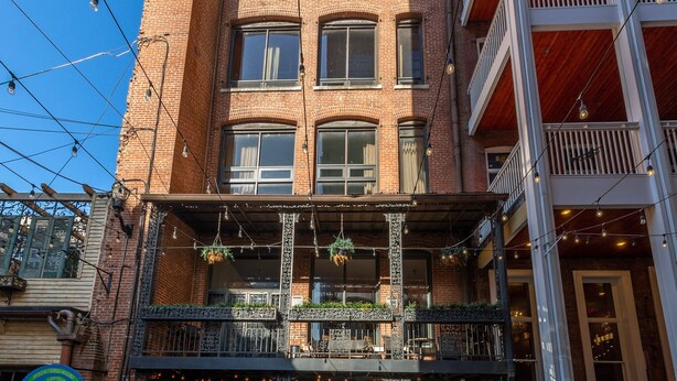 Un edificio a più piani con facciata in mattoni, un caffè con posti a sedere all'aperto al piano terra e una porta verde.