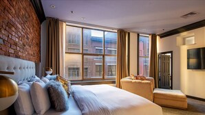 Camera d'albergo con un letto grande, un divano piccolo, un muro in mattoni e una finestra con tende.