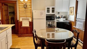 A kitchen with a round glass table and wooden chairs, white cabinets, a microwave, and a refrigerator. -  Charming West End 2BR. Dedicated parking. Private deck. Close to everything.. (provincetown)
