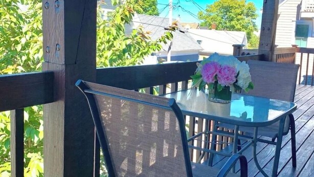 A covered outdoor area with a table and chairs, a glass top, and a vase with flowers. -  Charming West End 2BR. Dedicated parking. Private deck. Close to everything.. (provincetown)