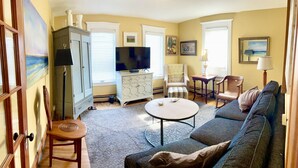 A living room with a sofa, a TV, a coffee table, and a cabinet. -  Charming West End 2BR. Dedicated parking. Private deck. Close to everything.. (provincetown)