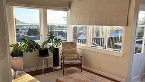 A cozy living room with a sofa, armchair, and ottoman, a large window with a view, and a wicker coffee table.