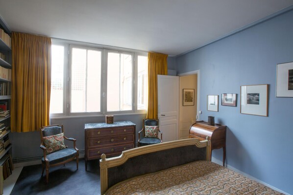 Une chambre à coucher comprenant un lit, deux chaises, une commode, un bureau et une bibliothèque.