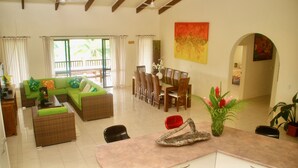 A spacious living area with a sofa set, dining table, chairs, and a kitchen counter. - Mataheres Upstairs Muri (Muri Beach)