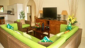 A living room with a green sofa, a wooden coffee table, a flat-screen TV, and a kitchen in the background. - Mataheres Upstairs Muri (Muri Beach)