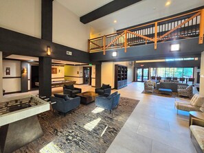 A spacious lobby with a pool table, comfortable seating, a staircase, and a view of the outdoors.