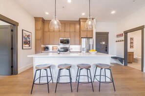 A modern kitchen with wooden cabinets, a central island with stools, pendant lighting, and a refrigerator.