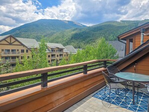 A balcony with a table and chairs, overlooking a mountainous landscape with buildings in the background.