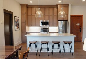 A modern kitchen with wooden cabinets, a central island with stools, stainless steel appliances, and pendant lighting. - Remodeled 2BR/3BA River Run Luxe • Vaulted Ceilings • Washer/Dryer • Sleeps 8 (Keystone)
