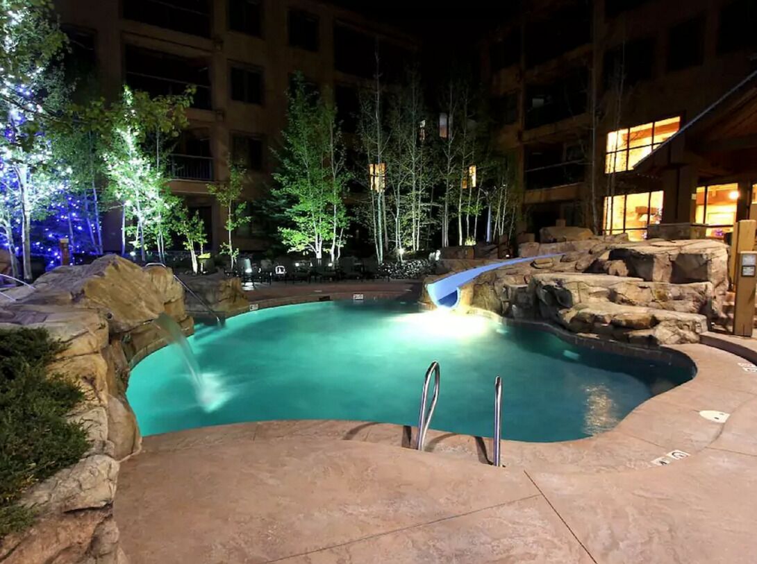 An indoor swimming pool with a waterfall feature, surrounded by trees and a stone wall.