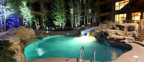 An indoor swimming pool with a waterfall feature, surrounded by trees and a stone wall.