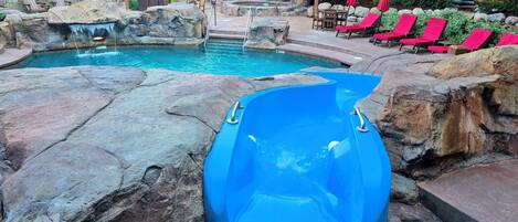 A pool area with a blue slide, lounge chairs, and a waterfall feature.
