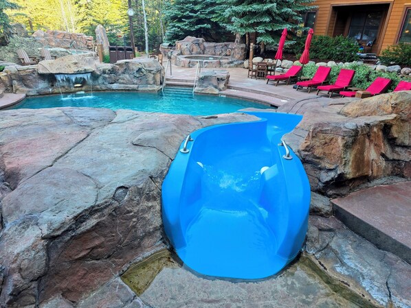 A pool area with a blue slide, lounge chairs, and a waterfall feature.