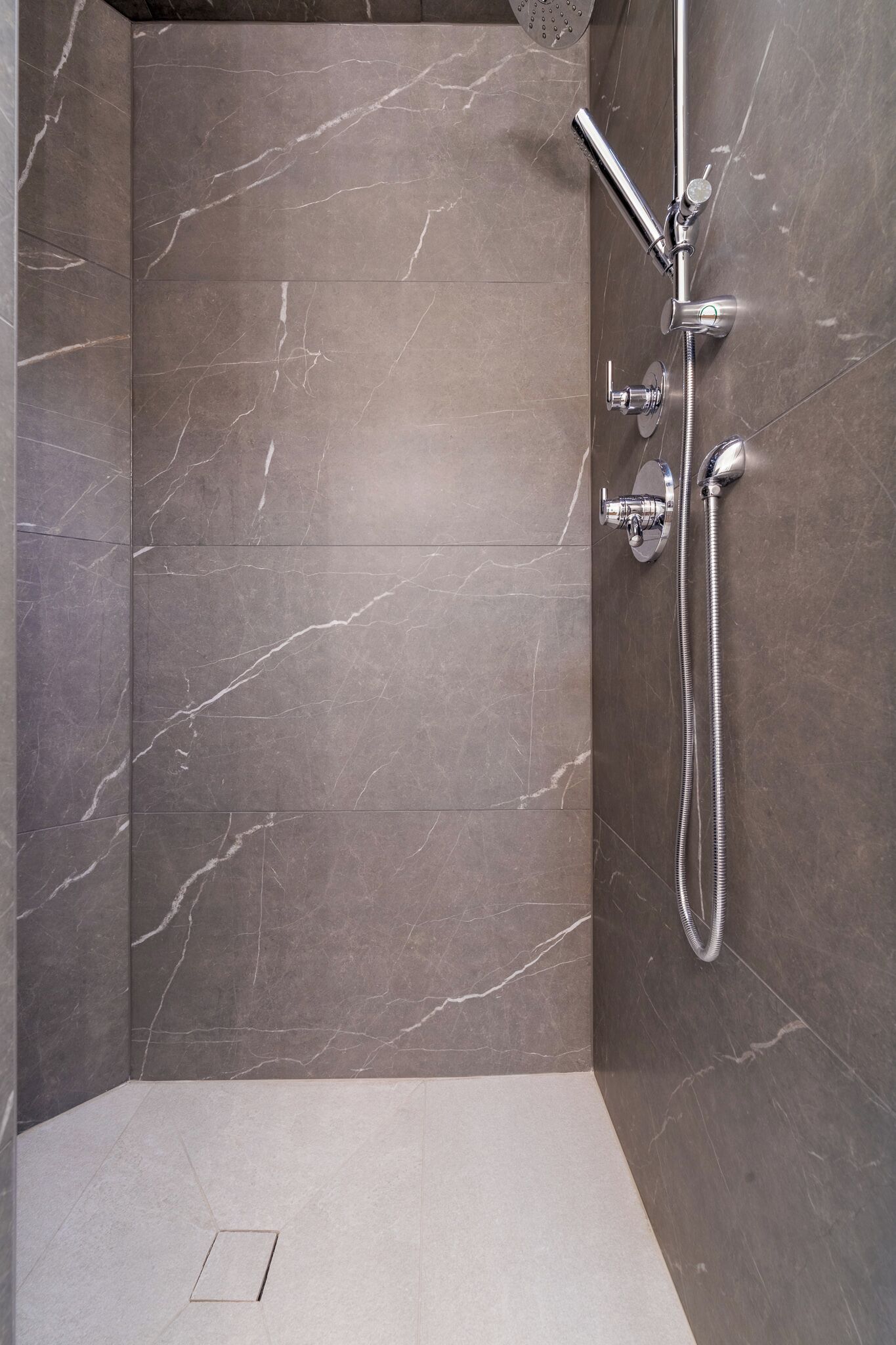 A modern shower with a handheld showerhead and a fixed wall-mounted faucet.