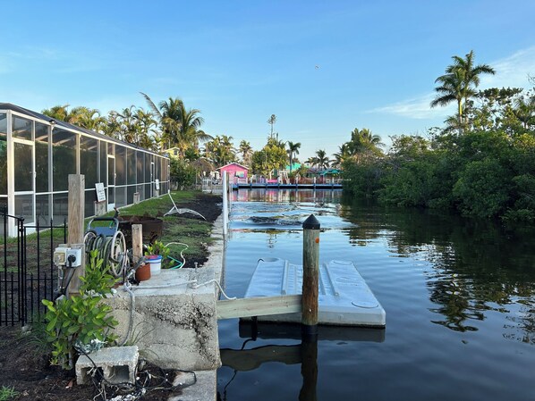A calm waterway with a dock, a greenhouse, and a row of houses in the background.