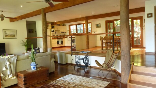 Uma sala de estar ampla com teto de madeira, uma área de refeições com mesa e cadeiras, e uma cozinha com armários brancos e fogão.